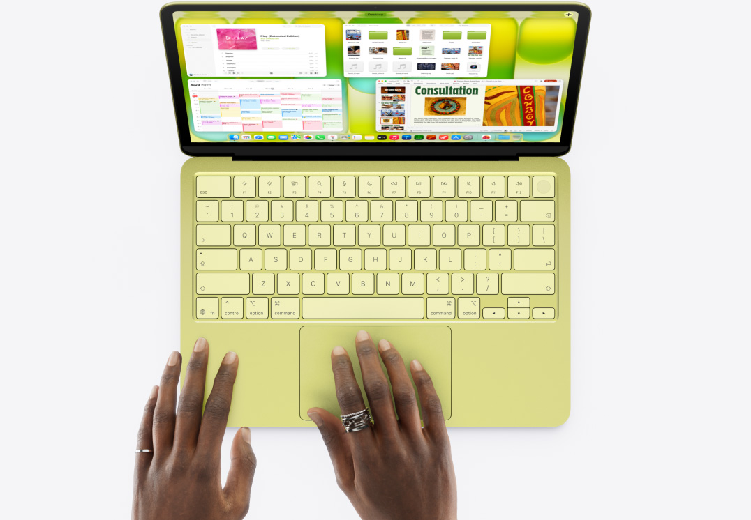 MacBook Neo, color cítrico, una mano en el trackpad, varias ventanas abiertas, incluidas las apps Música, Calendario y Microsoft PowerPoint