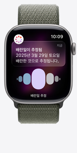 ‘건강’ 앱의 '생리 주기 추적'에서 배란일 추정 알림이 표시되고 Digital Crown이 보이는 스페이스 그레이 알루미늄 케이스 색상의 Apple Watch Series 11, 그리고 포레스트 스포츠 루프 밴드