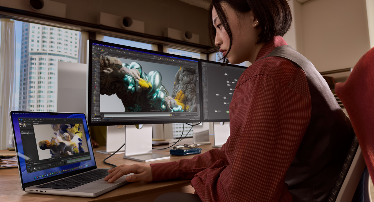 Bir ofis ortamında, Thunderbolt 5 bağlantı noktasıyla Studio Display XDR’a bağlı MacBook laptopta çalışan bir kişi