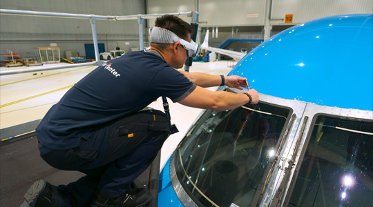 Ein Techniker in einem Flugzeughangar trägt die Apple Vision Pro und nutzt ein Tool, um die Windschutzscheibe des Flugzeugs zu justieren.