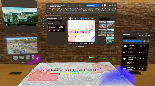 Eine 3D Projektion von Dashboards für Ersthelfer:innen zeigt Kameraaufnahmen, Teamzuweisungen und eine 3D Karte einer Parade-Route vor einer Backsteinwand in einem Büro