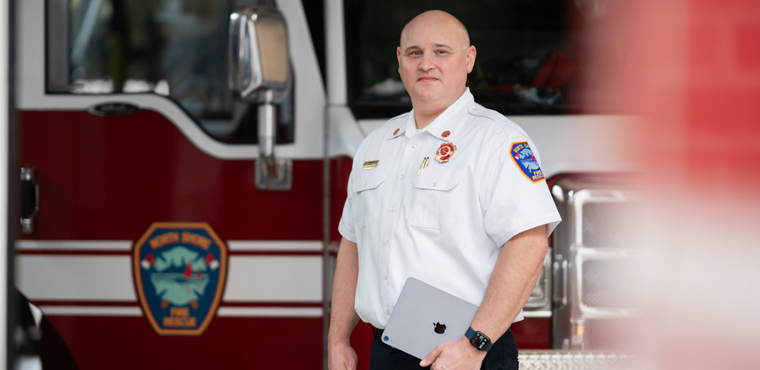 Der Feuerwehrchef steht vor einem Feuerwehrauto, hält ein iPad und trägt eine Apple Watch