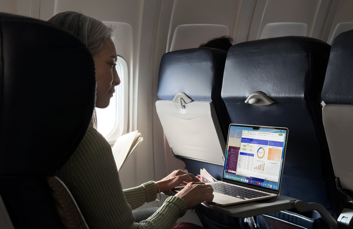 A person working on their MacBook Air while in an airplane seat