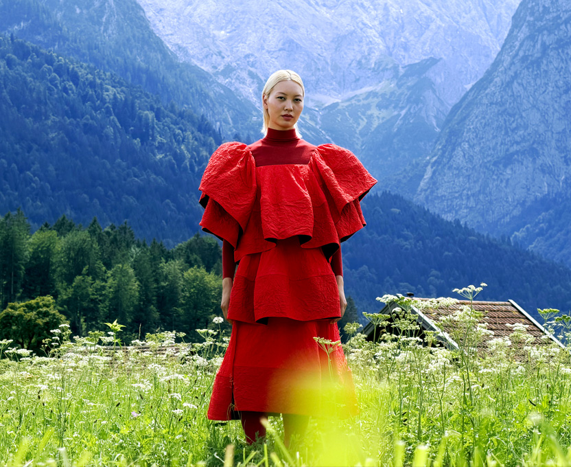 Modelo com vestido vermelho-vivo em um vale de montanhas mostrando a ampla tonalidade de cores do Studio Display XDR
