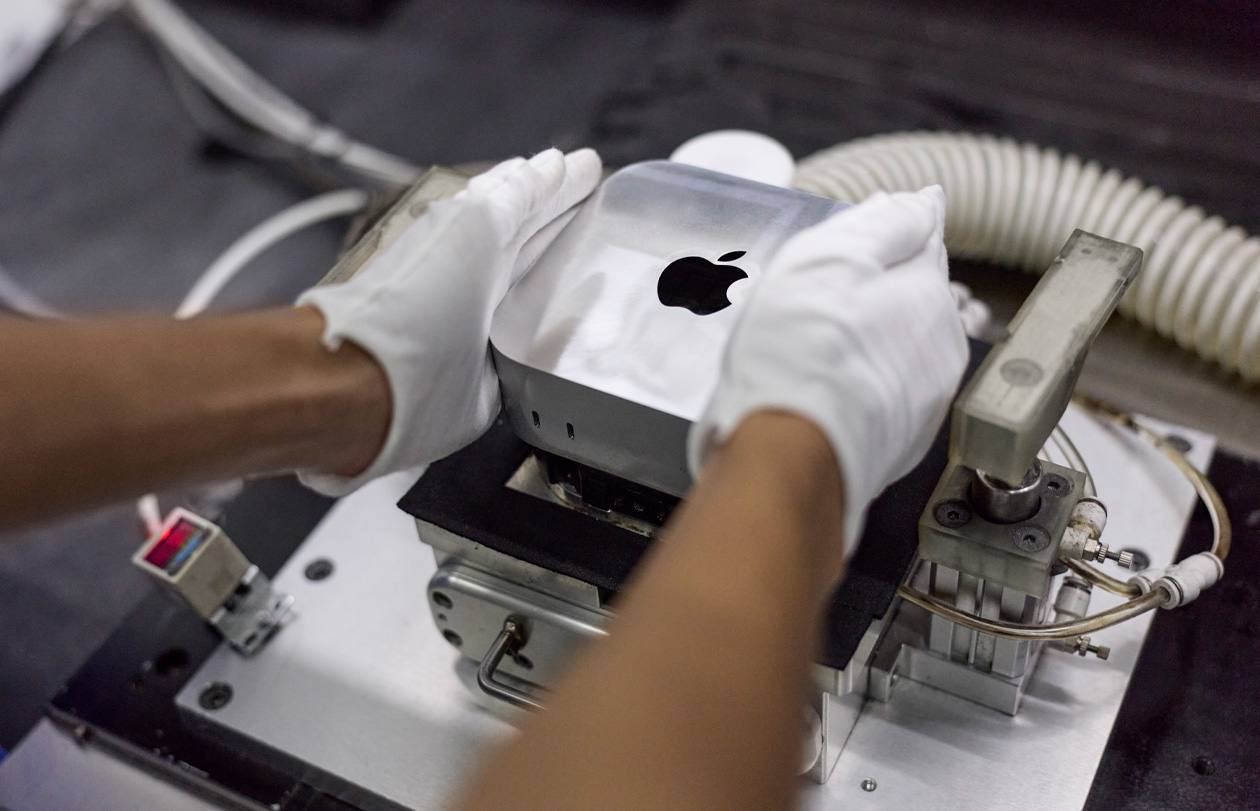 Behandschuhte Hände setzen während der Montage einen Mac mini in eine Fertigungsmaschine ein