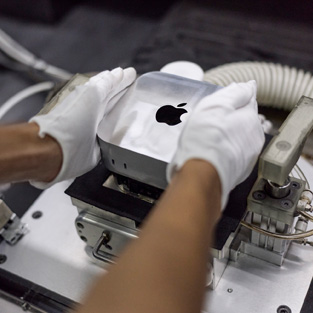 Behandschuhte Hände setzen während der Montage einen Mac mini in eine Fertigungsmaschine ein