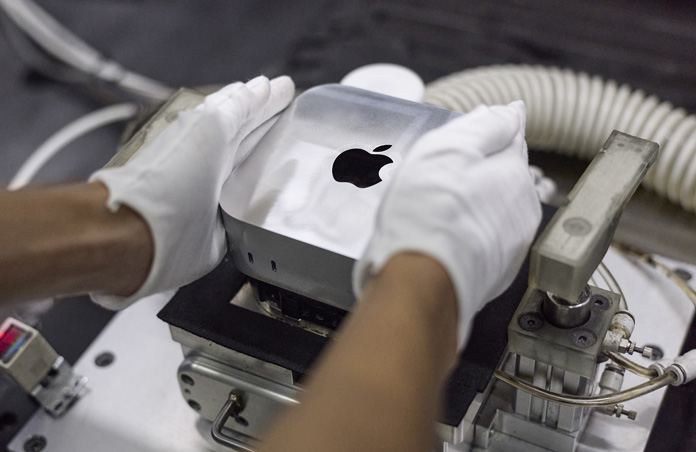 Behandschuhte Hände setzen während der Montage einen Mac mini in eine Fertigungsmaschine ein