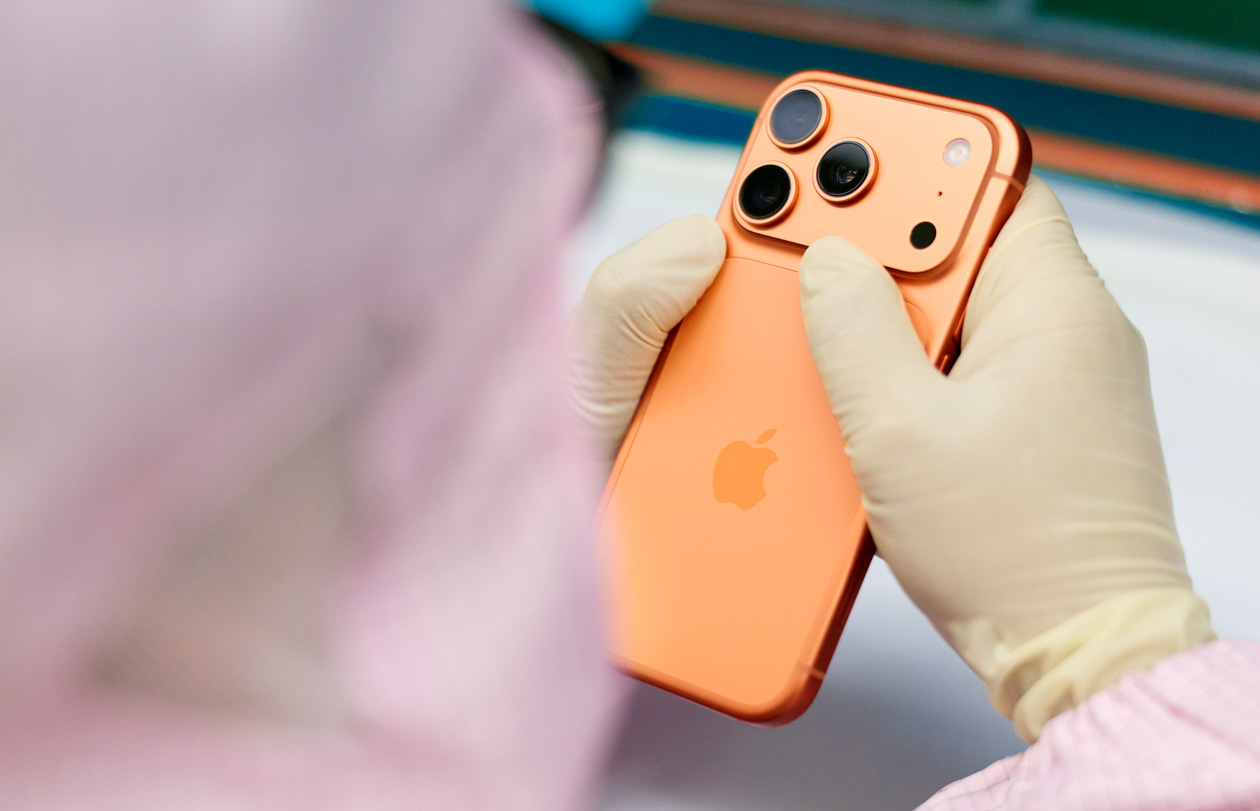 Eine Person in vollständiger Schutzkleidung prüft ein iPhone an einem Arbeitsplatz