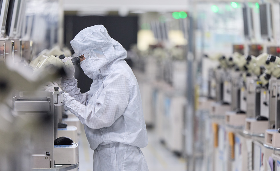 Eine Person in Arbeitskleidung mit Mundschutz drückt Tasten auf einer Produktionsmaschine