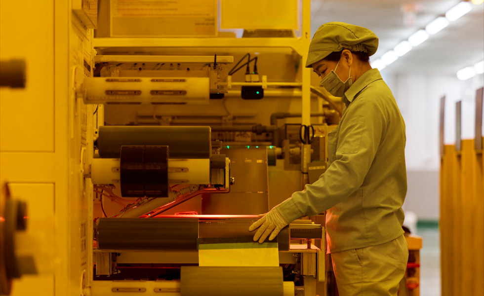 Eine Person in Arbeitskleidung mit Mundschutz drückt Tasten auf einer Produktionsmaschine
