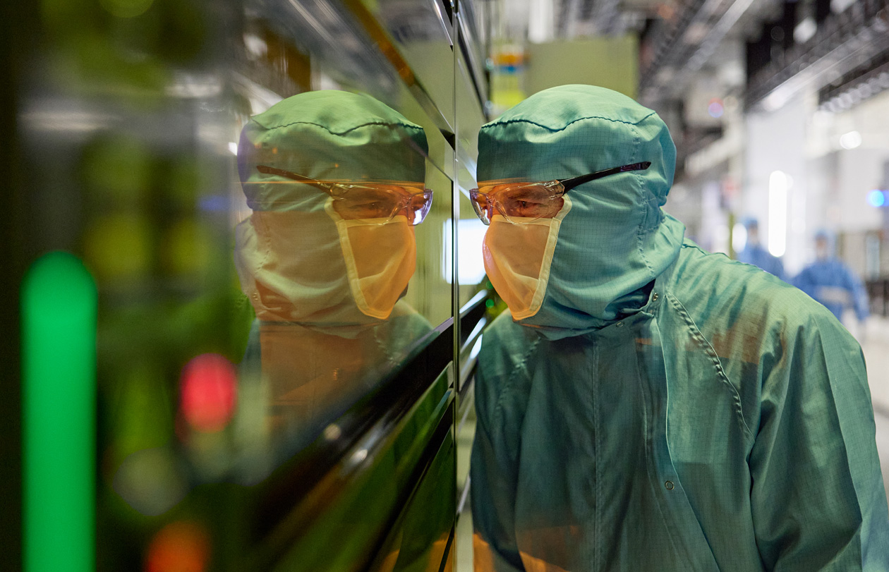 Ein Mitarbeiter in einem Ganzkörperanzug schaut durch ein Fenster in eine Produktionsmaschine