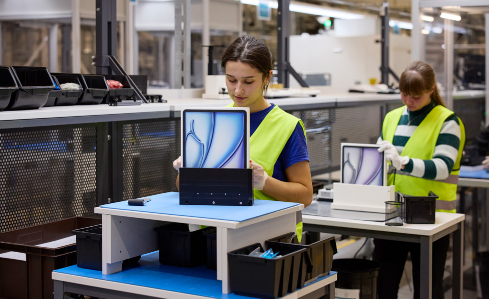 Zwei Mitarbeitende mit Sicherheitswesten sitzen an ihren Arbeitsplätzen mit Produktverpackungen