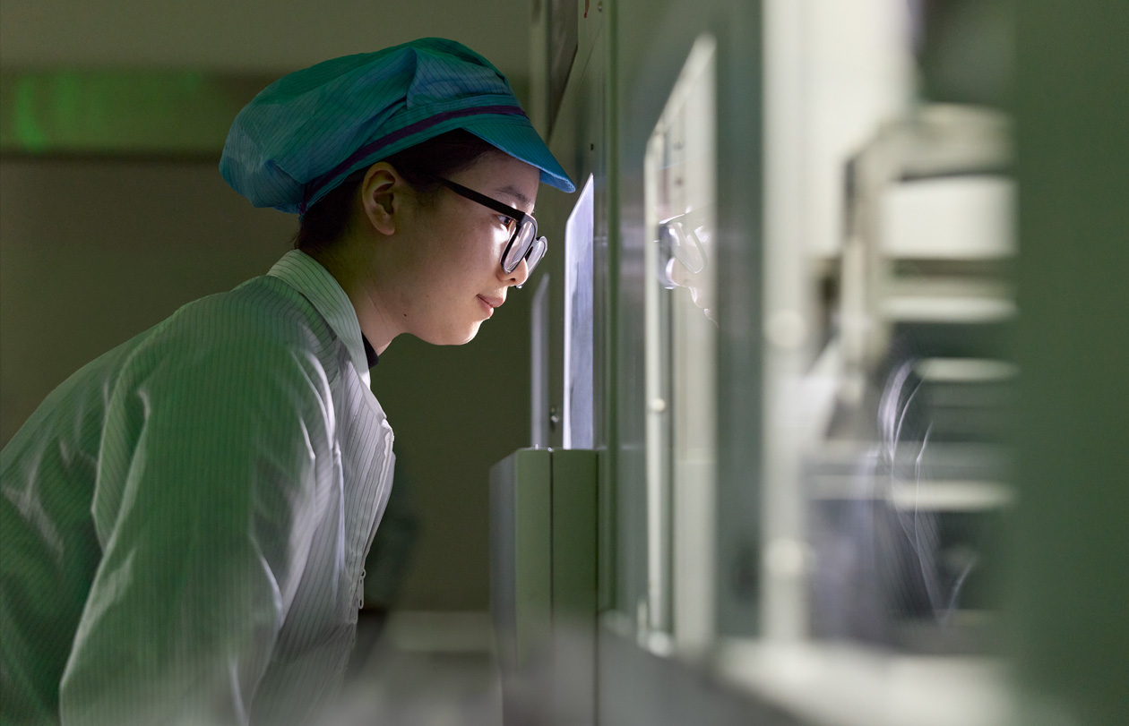 Eine Mitarbeiterin in vollständiger Schutzkleidung und mit Schutzbrille beobachtet die Montage der Apple Watch