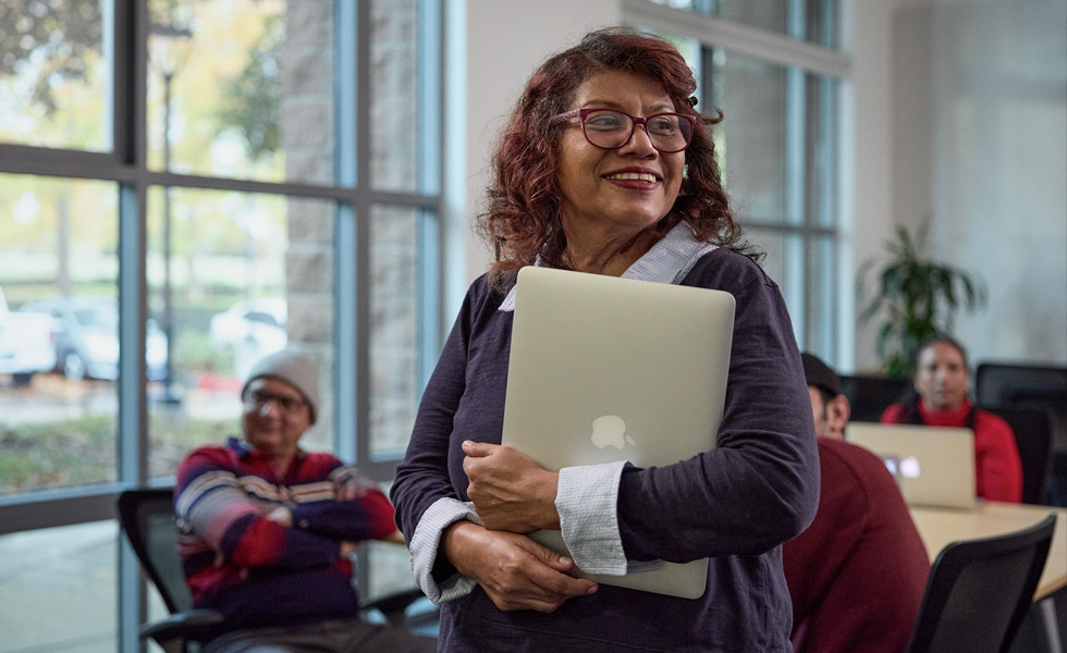 Eine Frau trägt ihren Laptop vor ein Klassenzimmer oder eine Lernumgebung