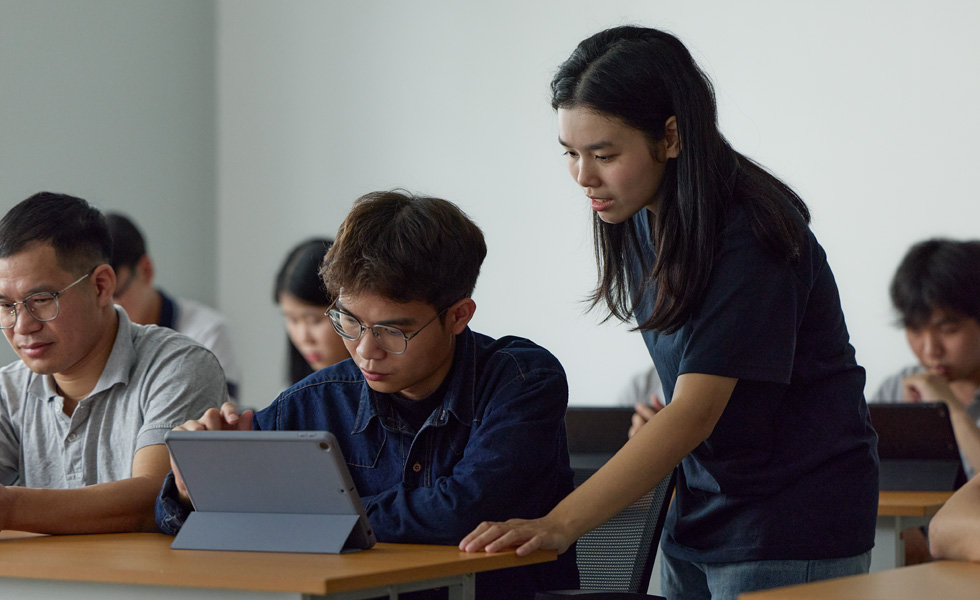 Zwei Personen in einem Klassenzimmer arbeiten an einem Apple Tablet zusammen