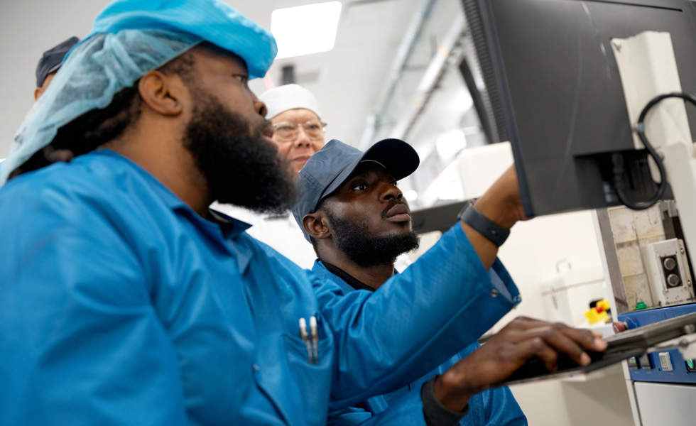 Eine Gruppe von Mitarbeitenden in Arbeitskleidung arbeitet gemeinsam vor einem Monitor