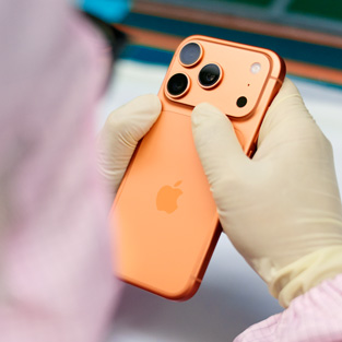 Eine Person in vollständiger Schutzkleidung prüft ein iPhone an einem Arbeitsplatz