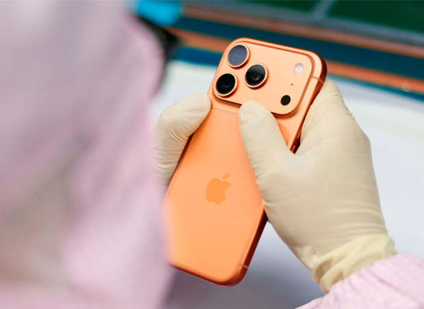 Eine Person in vollständiger Schutzkleidung prüft ein iPhone an einem Arbeitsplatz